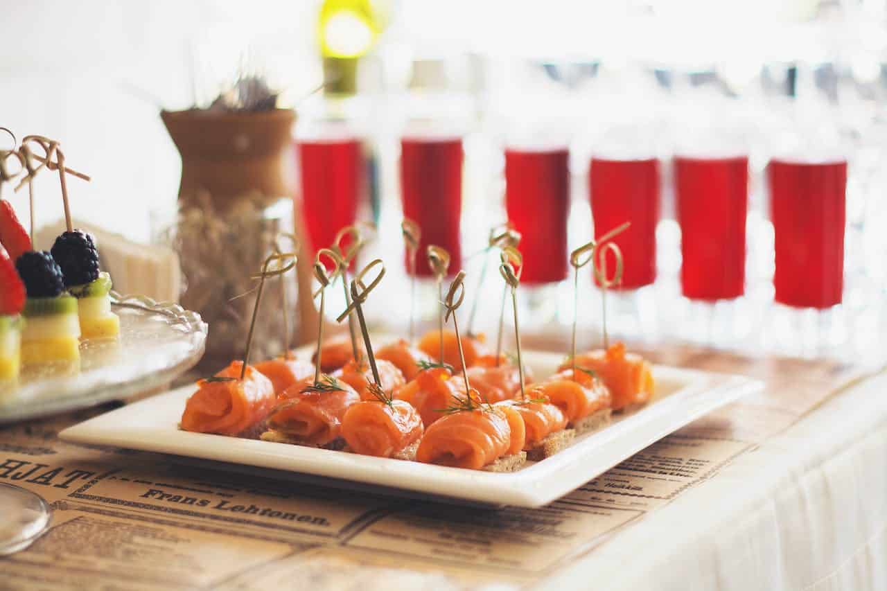 Image title: A table topped with white plates filled with delectable delicacies. Image alt-text: gourmet catering trends Photo by Tanya Gorelova: https://www.pexels.com/photo/salmon-canapes-and-fruits-on-white-tray-3933162/